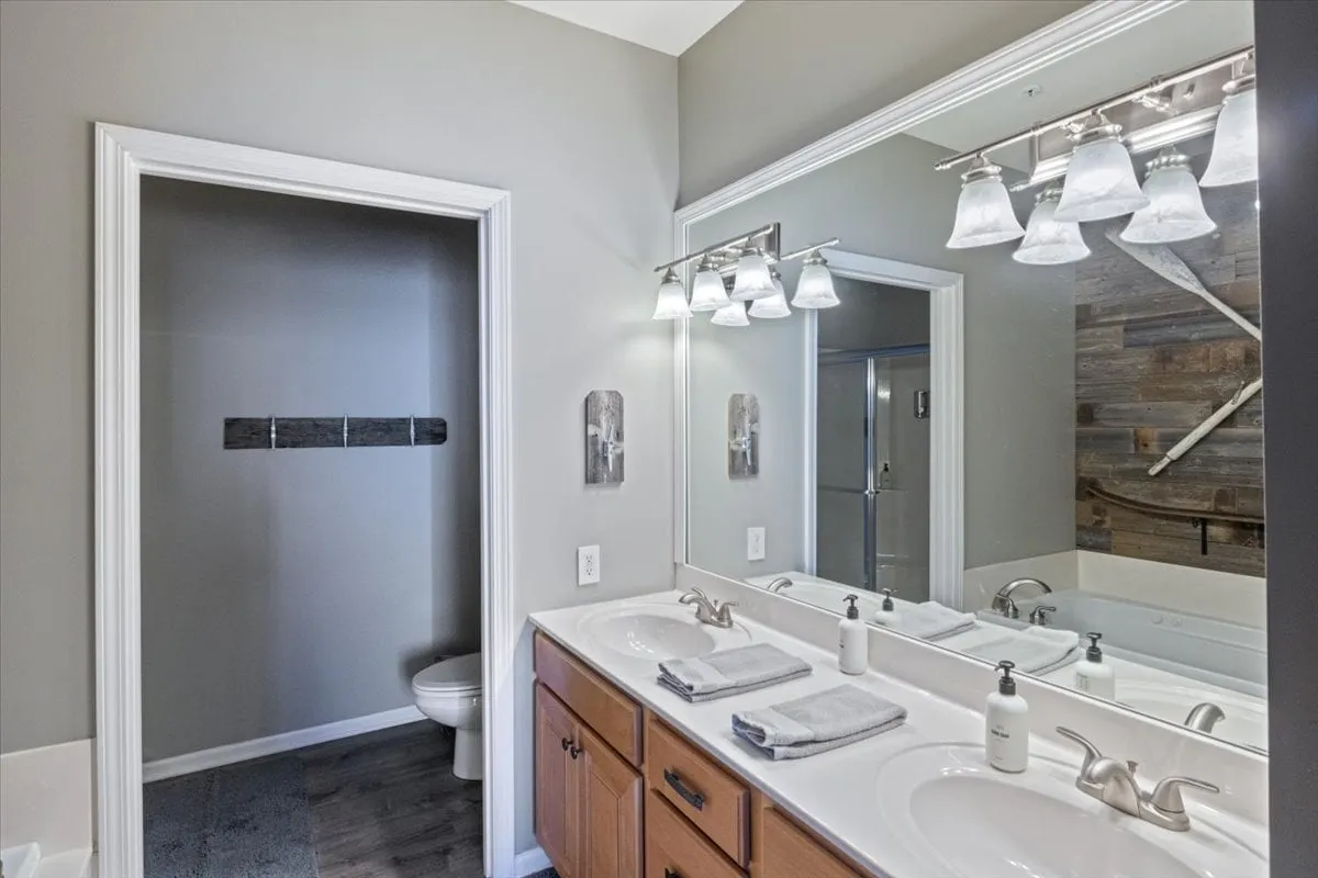 A modern bathroom scene with a double vanity, two mirrors, stylish lighting fixtures, and warm wood accents, creating a spa-like and tranquil environment for personal care.