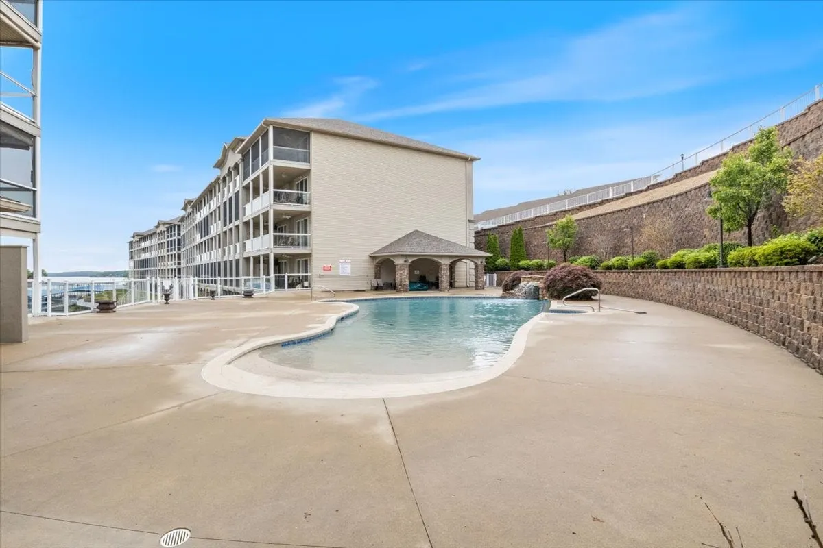 A vibrant outdoor swimming pool surrounded by lush greenery and the lodge’s building architecture, with several lounge chairs positioned poolside. The water glimmers in the sunlight, inviting guests to unwind or socialize in a resort-like setting.