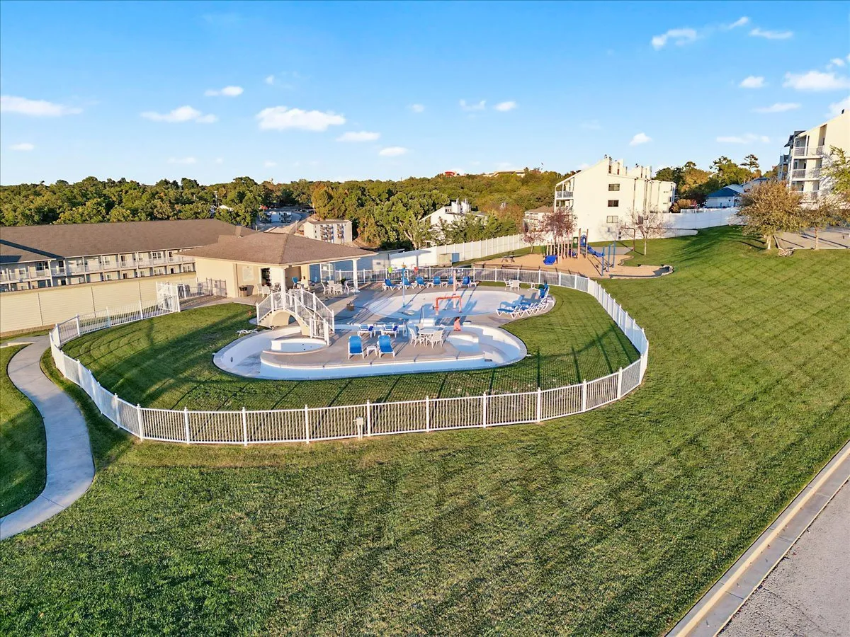 This exterior image captures the heart of the Lands End community's resort-style amenities with a clear view of the swimming pool, lounge chairs for sunbathing, and the playground in the background. Children can be seen playing, while others relax poolside, emphasizing the area's family-friendly and fun atmosphere.