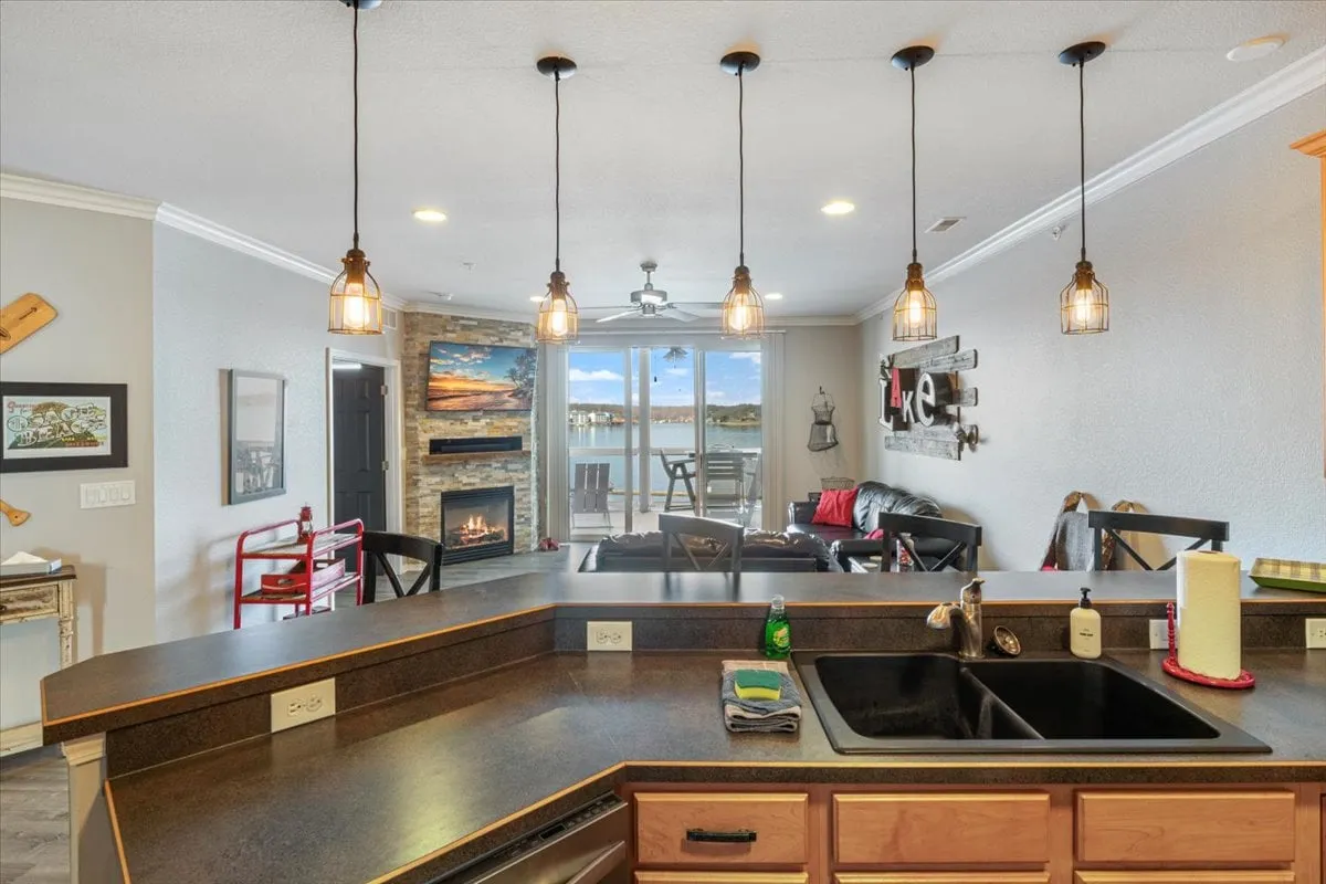 This image captures an open-plan interior space featuring a central kitchen island, a cozy fireplace, and expansive windows that overlook a tranquil lake. The natural light floods the room, and the inviting seating areas suggest a place for both relaxation and social gatherings. Decorative wall art and warm finishes add to the welcoming ambience.