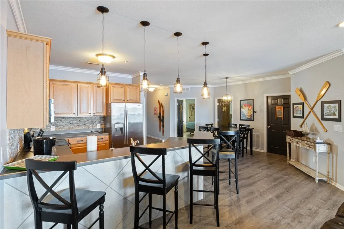 A welcoming kitchen featuring a spacious island with bar stools, pendant lighting, and stainless steel appliances. The scene is styled for entertaining and casual dining, with an inviting, open layout ideal for groups or families. The amenities and thoughtful design evoke a sense of comfort and preparedness.