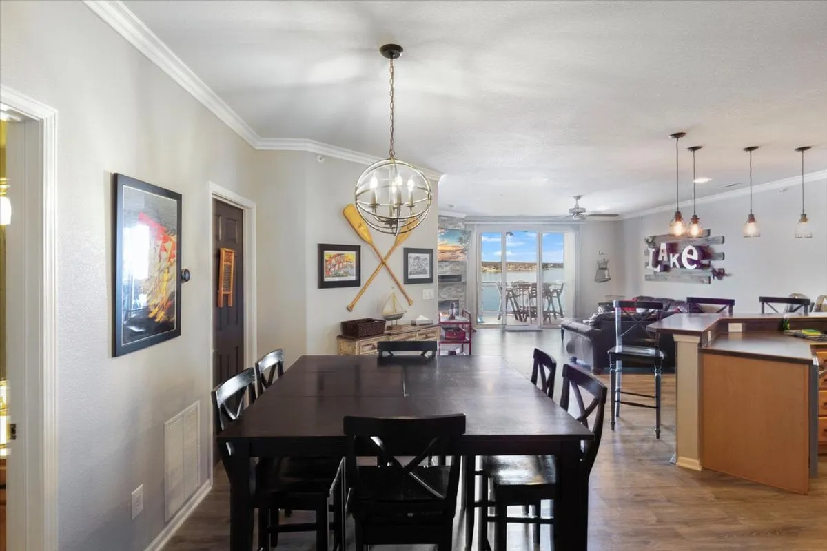 A long dining table is set before large windows, offering a stunning view of the shimmering lake beyond. The space is complemented by warm pendant lighting and decorative wall art, fostering an inviting atmosphere for shared meals, celebrations, and sunset watching.