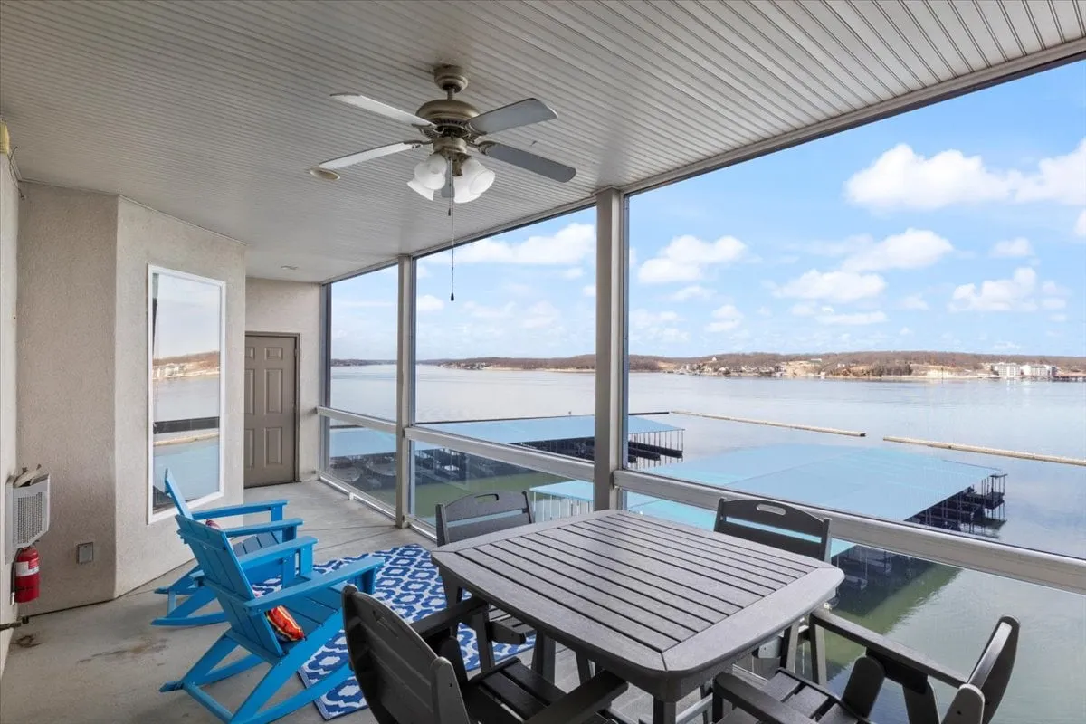 A spacious outdoor dining area with blue chairs and a table, set under a ceiling fan and overlooking a serene lake. The setting is ideal for group meals, casual conversations, and enjoying the fresh air while surrounded by scenic beauty.