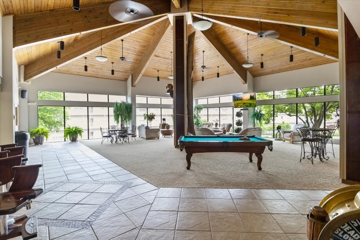 This inviting interior shot of the clubhouse focuses on a pool table, comfortable seating, and large windows that let in natural light. The relaxed environment is ideal for socializing and friendly games, appealing to families and groups of friends.