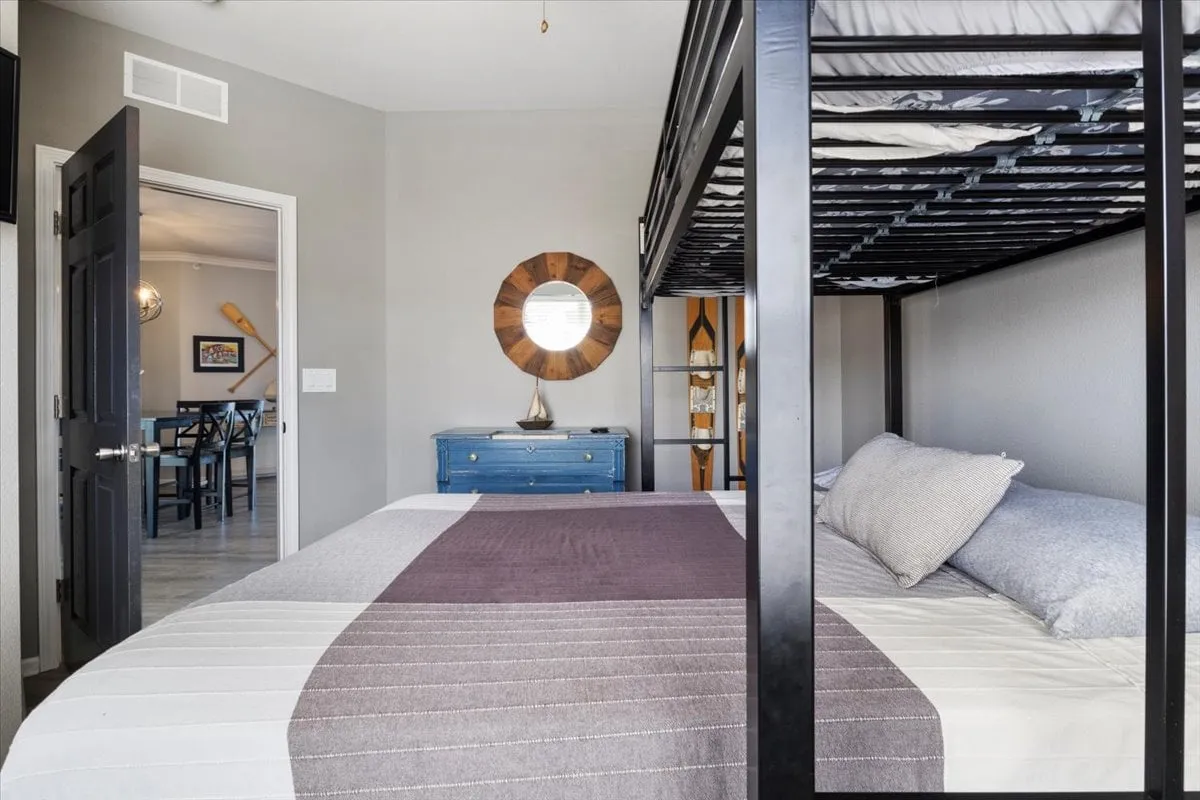 A cozy and functional secondary bedroom with a bunk bed, blue dresser, circular mirror, and textured bedding. The room’s inviting setup is perfect for families or groups, emphasizing both comfort and flexibility.