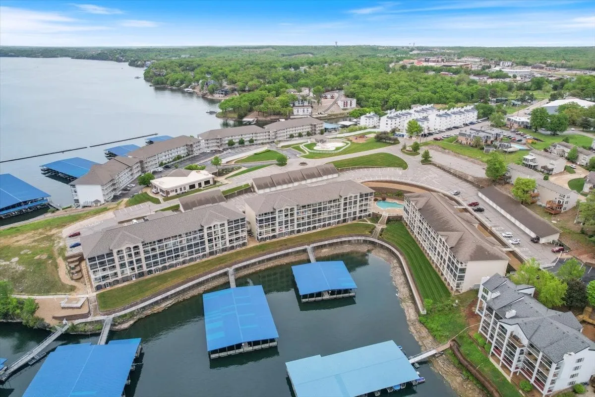 This exterior shot captures an expansive view of the lake, a modern marina with blue boat covers, lush landscaping, and stylish residential buildings. The image exudes a vibrant, active lakeside community, showcasing the boating facilities and the beautiful natural surroundings of Lake of the Ozarks.