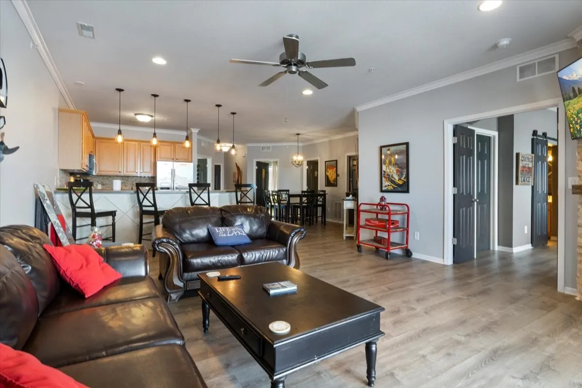 A cozy open-concept living and dining area, with a leather sofa, coffee table, visible kitchen bar, and dining table. The scene is styled for relaxation, entertaining, and family gatherings, reflecting a homey yet elevated ambiance.