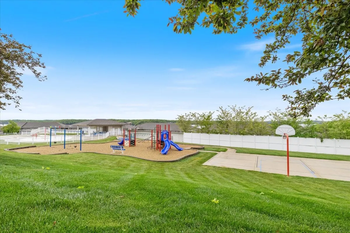 A vibrant playground with modern equipment, a basketball court, and open green spaces. Children are playing, and families can be seen gathering in the background, creating a joyful, active scene.